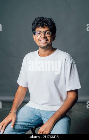 Young man sitting on chair in front of gray backdrop Stock Photo