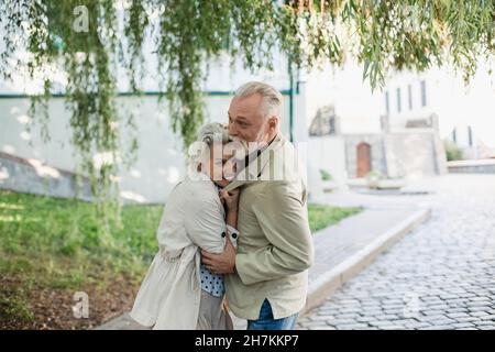 Smiling senior woman embracing man on footpath Stock Photo
