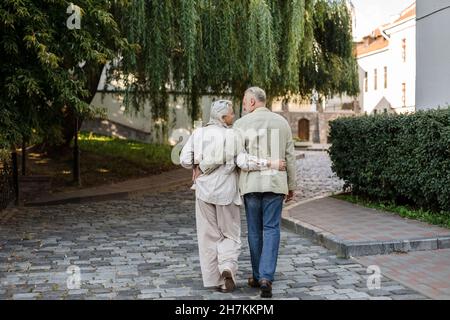 Couple with arms around walking at city street Stock Photo