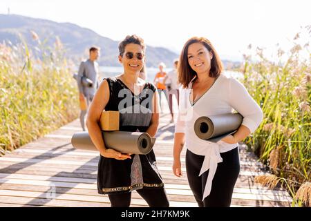 Women with exercise mats standing on jetty at yoga class Stock Photo