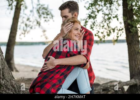 Young man embracing smiling girlfriend at beach Stock Photo