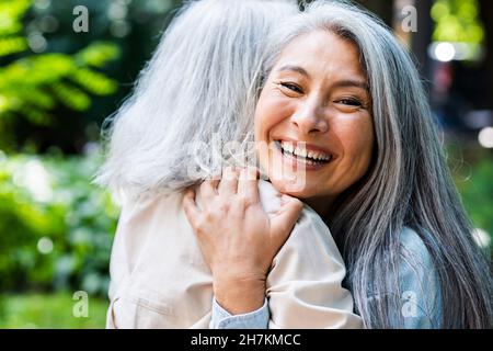 Happy mature woman with gray hair hugging female friend Stock Photo