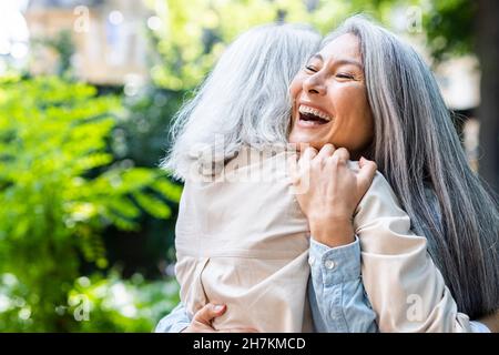 Mature women laughing while hugging female friend Stock Photo