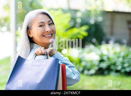 Happy mature woman looking over shoulder while carrying shopping bags Stock Photo