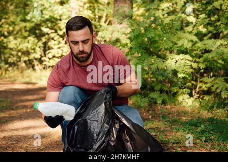 Male volunteer putting plastic bottle in garbage bag Stock Photo