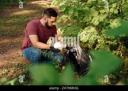 Male activist putting plastic bottle in garbage bag Stock Photo