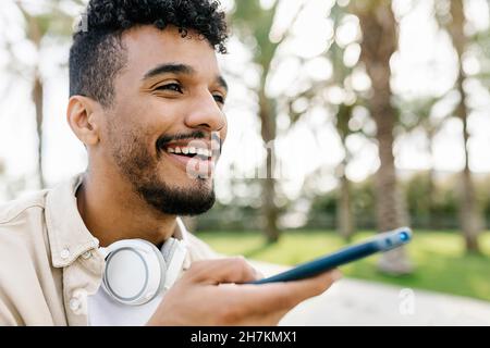 Smiling man with wireless headphones talking through speaker on smart phone Stock Photo