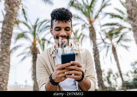 Smiling young man with black hair using smart phone Stock Photo