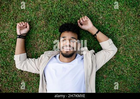 Happy young man with eyes closed relaxing on grass Stock Photo