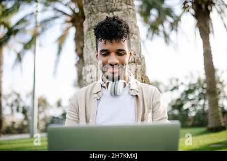 Bearded man with wireless headphones using laptop at park Stock Photo
