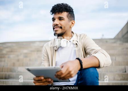 Bearded man holding digital tablet while sitting on steps Stock Photo