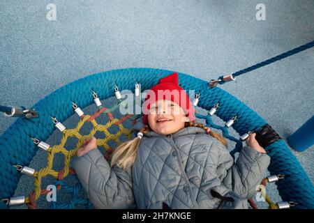 Smiling girl lying on nest swing in playground Stock Photo