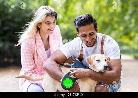 Smiling young man embracing dog by girlfriend in park Stock Photo