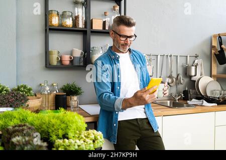 Man with coffee cup using mobile phone in kitchen at home Stock Photo