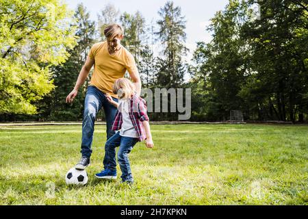 Father and son playing with soccer ball at park Stock Photo