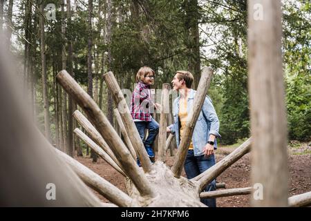 Father looking at son standing on tree trunk in forest Stock Photo