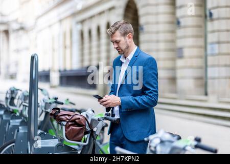 Young businessman using mobile phone at bicycle parking station Stock Photo