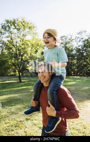 Father carrying cheerful son on shoulders in park Stock Photo