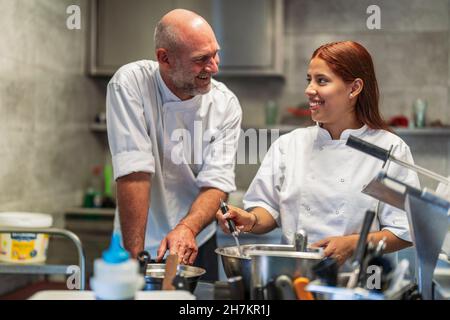 Smiling male and female chefs talking while cooking in kitchen Stock Photo