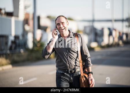 Cheerful businessman talking on smart phone while going for work Stock Photo