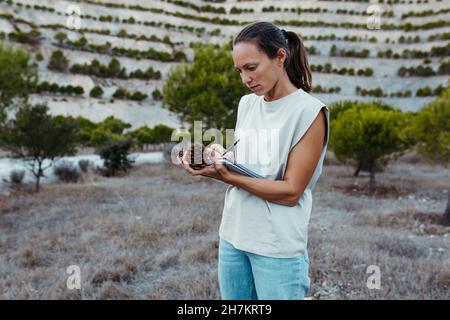 Female expertise collecting data of pine cones in book at old mine Stock Photo