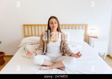 Young woman meditating while on bed at home Stock Photo