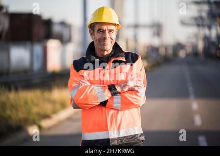 Smiling male dock worker with arms crossed on street at industry Stock Photo