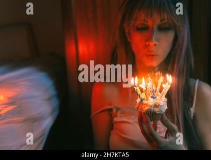 Young woman blowing burning candles on birthday cupcake at home Stock Photo