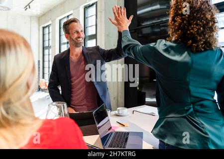 Smiling businessman giving high-five to colleague in meeting Stock Photo