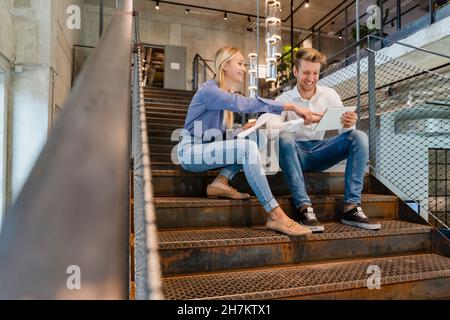 Young coworkers using tablet PC on staircase in office Stock Photo