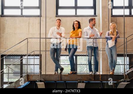 Coworkers having discussion at railing in office Stock Photo
