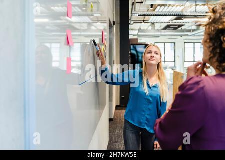 Young businesswoman explaining graph to colleague at whiteboard Stock Photo