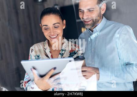 Smiling businesswoman with tablet PC by colleague seen through window Stock Photo