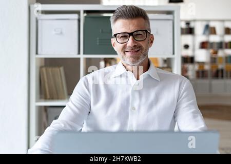 Smiling businessman with laptop contemplating in office Stock Photo