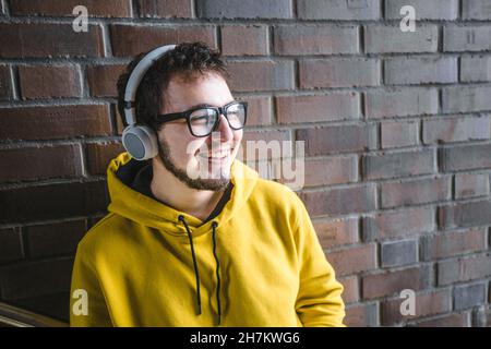 Smiling student with bag listening music in front of brick wall Stock Photo