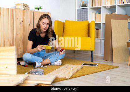 Smiling young woman with screwdriver using mobile phone in living room Stock Photo
