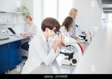 Researcher using microscope with colleagues working in background Stock Photo