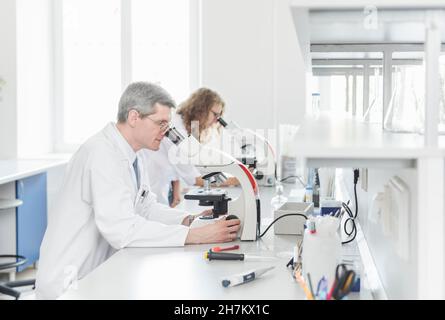 Scientists researching through microscope in laboratory Stock Photo