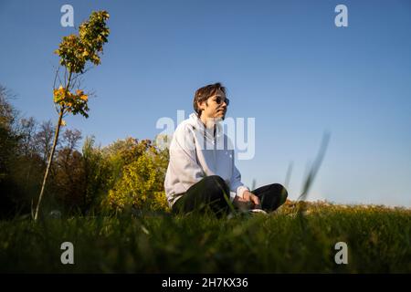 Man wearing sunglasses sitting cross-legged on grass Stock Photo