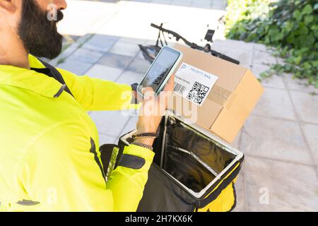 Delivery man with mobile phone holding package in public park Stock Photo