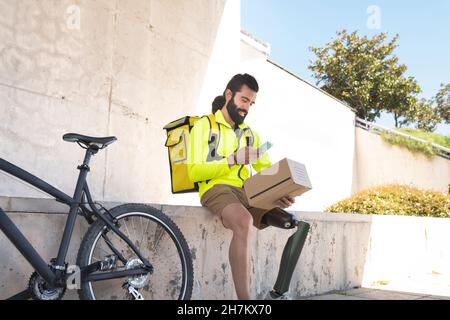 Bearded delivery man with prosthetic leg holding package on wall Stock Photo