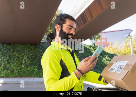 Bearded delivery man scanning QR code through smart phone on footpath Stock Photo