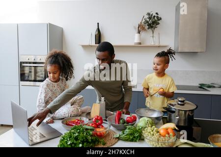 Smiling father using laptop amidst son and daughter in kitchen Stock Photo