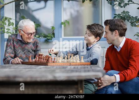 Man looking at father playing chess with son in backyard Stock Photo