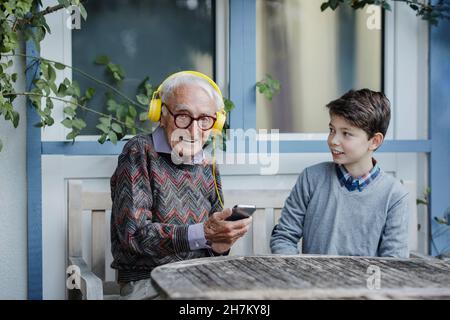 Smiling boy looking at grandfather listening music through headphones in backyard Stock Photo