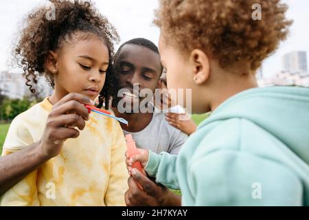 Father holding bubble wand with children at park Stock Photo