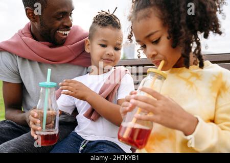 Father looking at children drinking lemonade in park Stock Photo