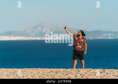 Young man taking selfie through smart phone at beach, Tarifa, Spain Stock Photo