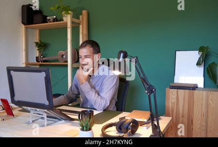 Smiling businessman with hand on chin using laptop Stock Photo