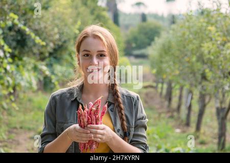 Smiling beautiful female farmer holding fresh beans in garden Stock Photo